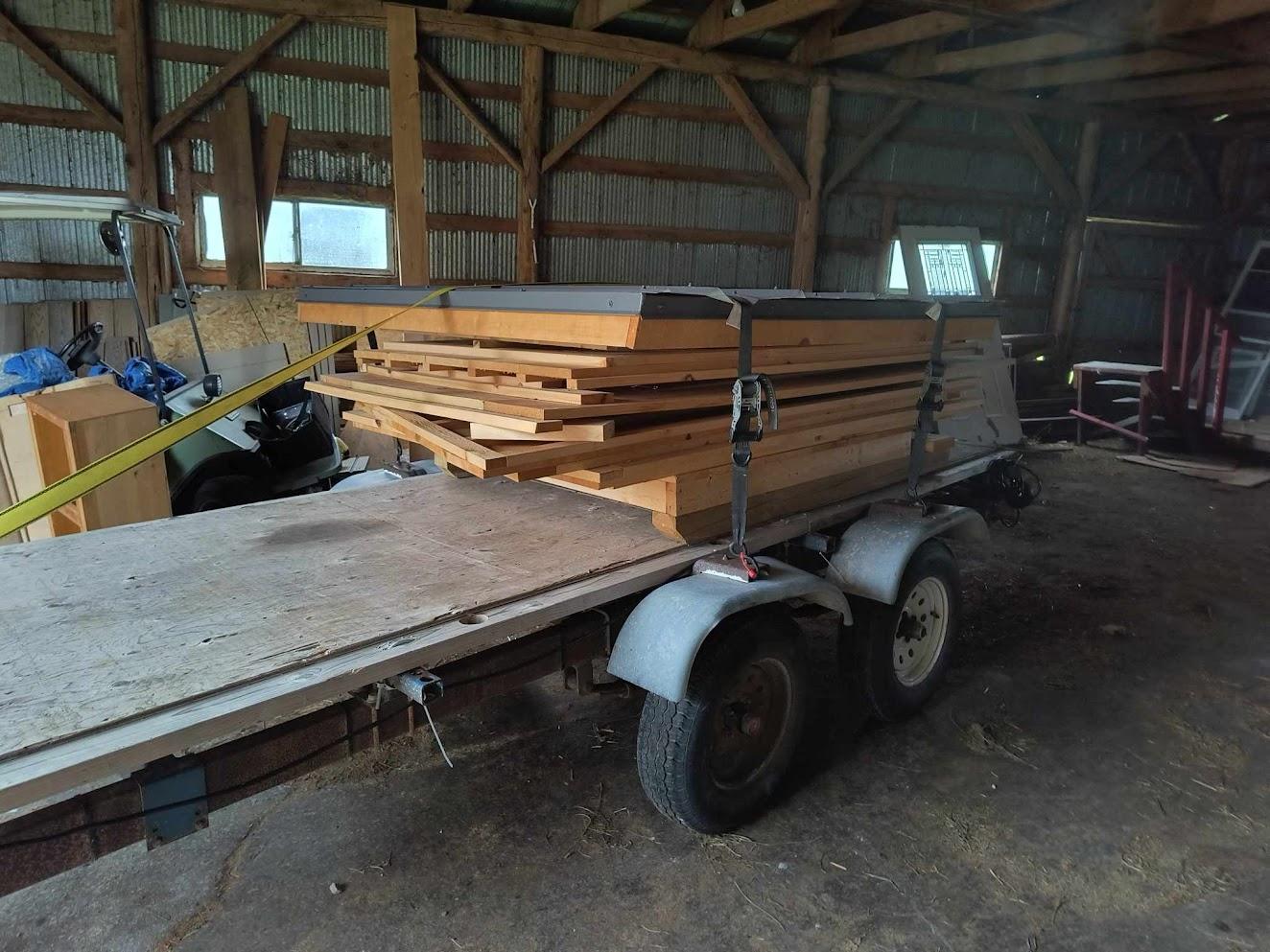 Flat pack outhouse sections secured on a tandem trailer inside a barn, ready for transport in Ontario